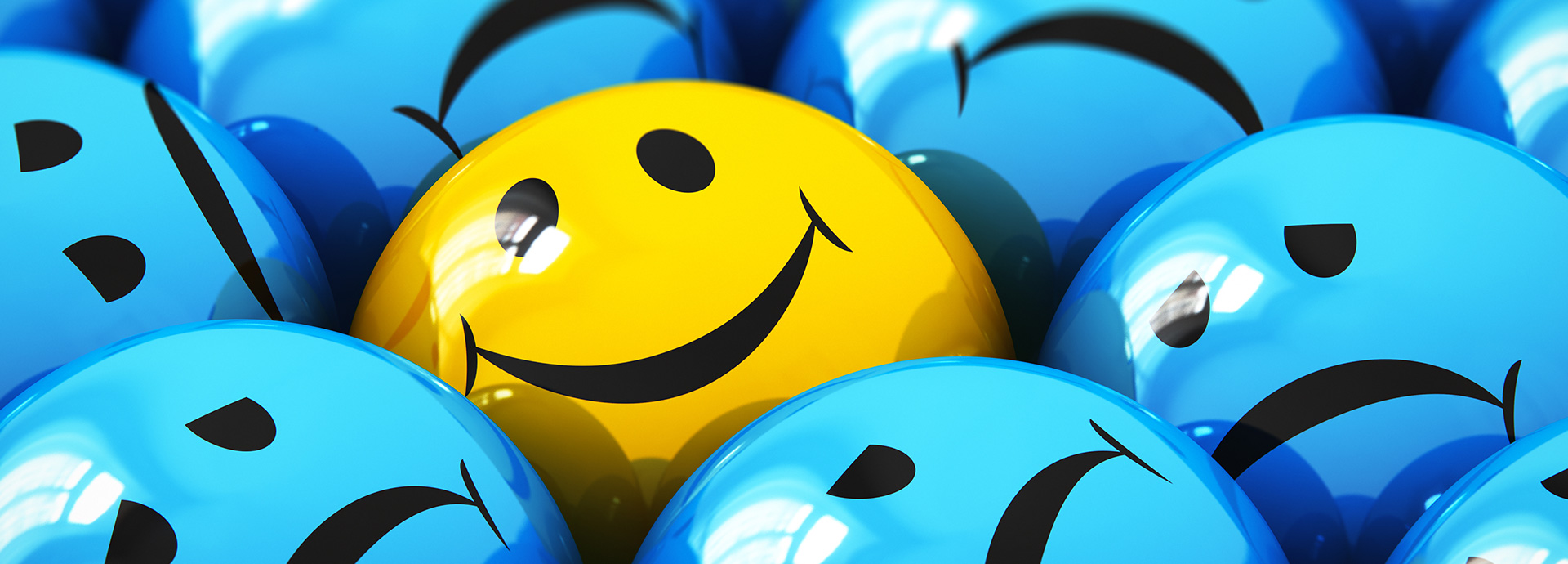 Gelber Smiley-Ball hebt sich zwischen vielen blauen traurigen Bällen ab.