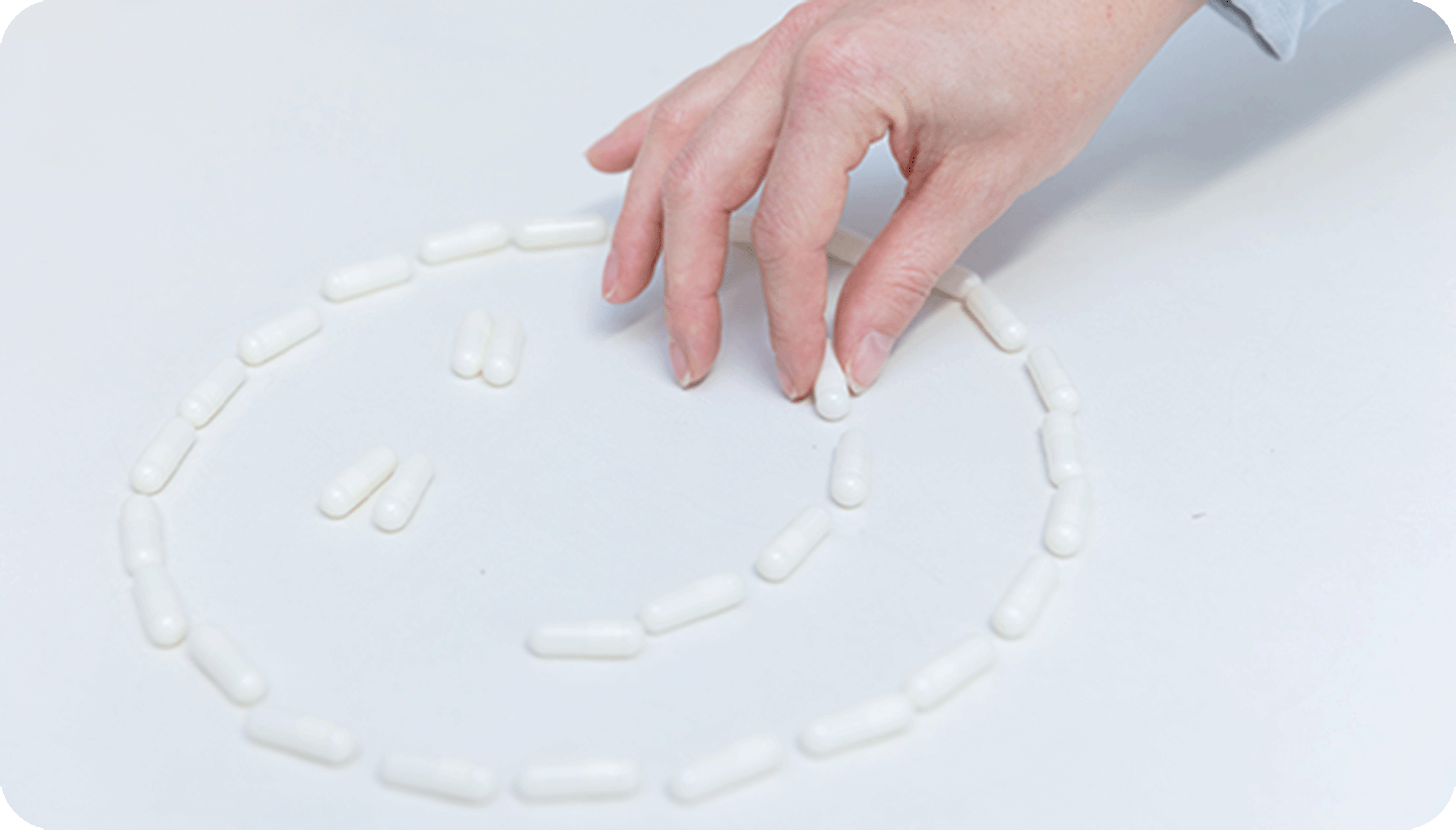 Hand ordnet weiße Kapseln zu einem Smiley an.