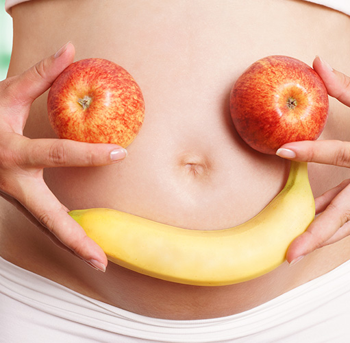 Auf einem Bauch liegen zwei Äpfel und eine Banane als Smiley.