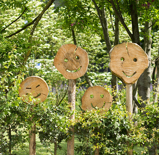 Vier Holzscheiben mit geschnitzten Smiley-Gesichtern im Garten.